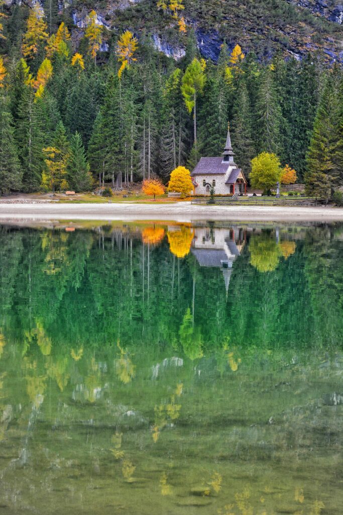 Charming church amidst colorful autumn foliage reflecting in tranquil lake.